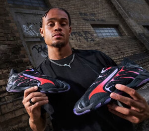 A man holding a pair of black and purple Puma sneakers